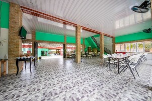 A spacious hall with high ceilings, green walls, and a tiled floor. There are tables and chairs arranged for meetings or dining.