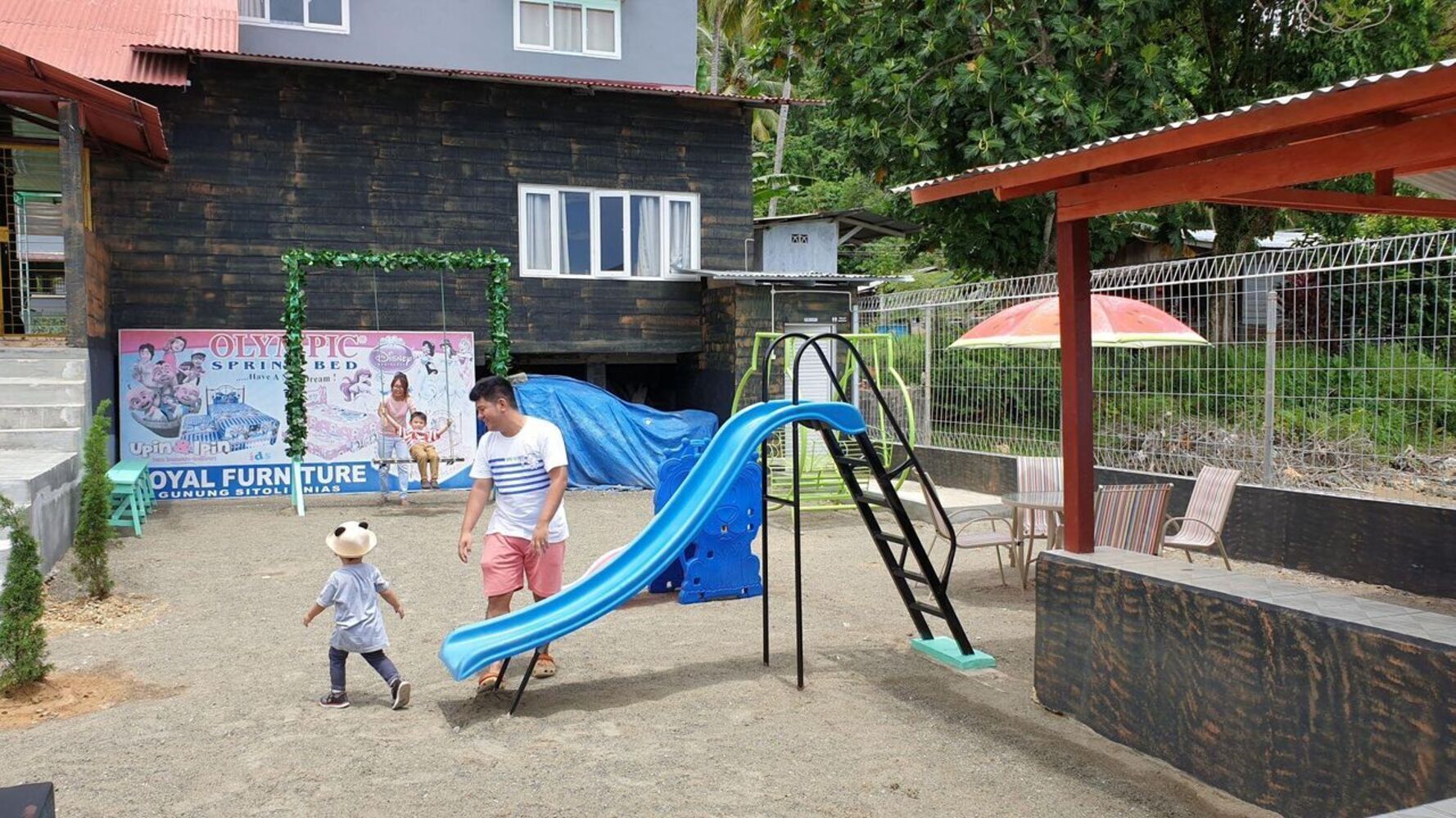 A playground with a blue slide and a man and child nearby.