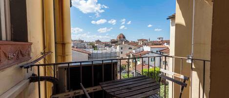 A balcony with a wooden table and metal railing, overlooking a cityscape with buildings and a dome structure.
