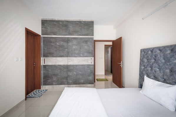 A modern bedroom with a large bed, a grey tufted headboard, and a grey and white accent wall.