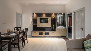 A dining area with a table set for four, a television mounted above the table, and a cabinet with a mirror and decorative items. - The Galleria Home by Red Olive Yelahanka (Bengaluru)