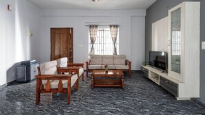 A living room with a sofa, two armchairs, a coffee table, a TV on a wooden stand, and a window with curtains. - The Nebula by Red Olive (Bengaluru)