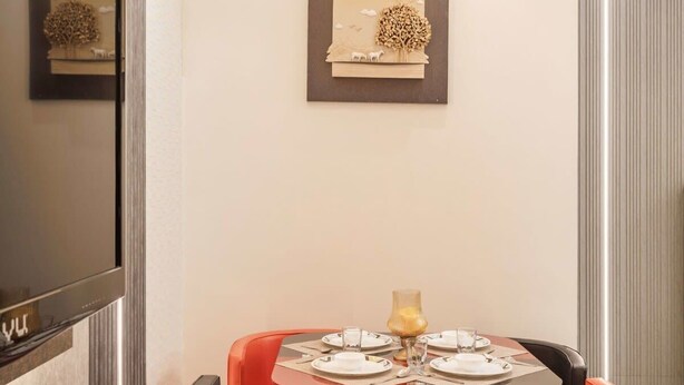 A modern dining area with a round table, red and black chairs, a flat-screen TV, and artwork on the walls.