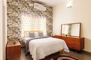 A bedroom with a stone-patterned wall, a bed with a white quilt, a wooden dresser, and a mirror.