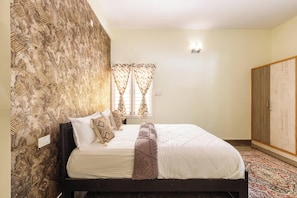A bedroom with a bed, patterned wallpaper, a window with curtains, and a wardrobe.