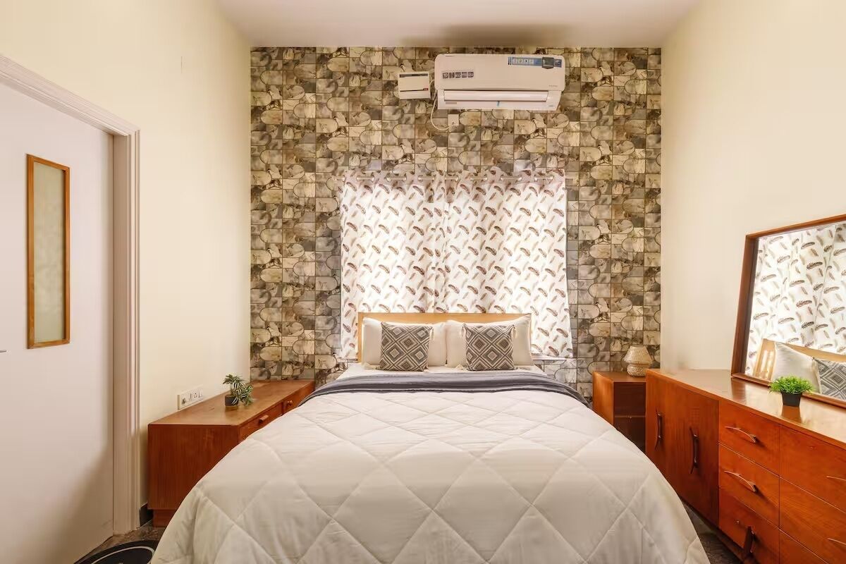 A bedroom with a bed, a dresser, a nightstand, an air conditioner, and a stone-patterned wall.