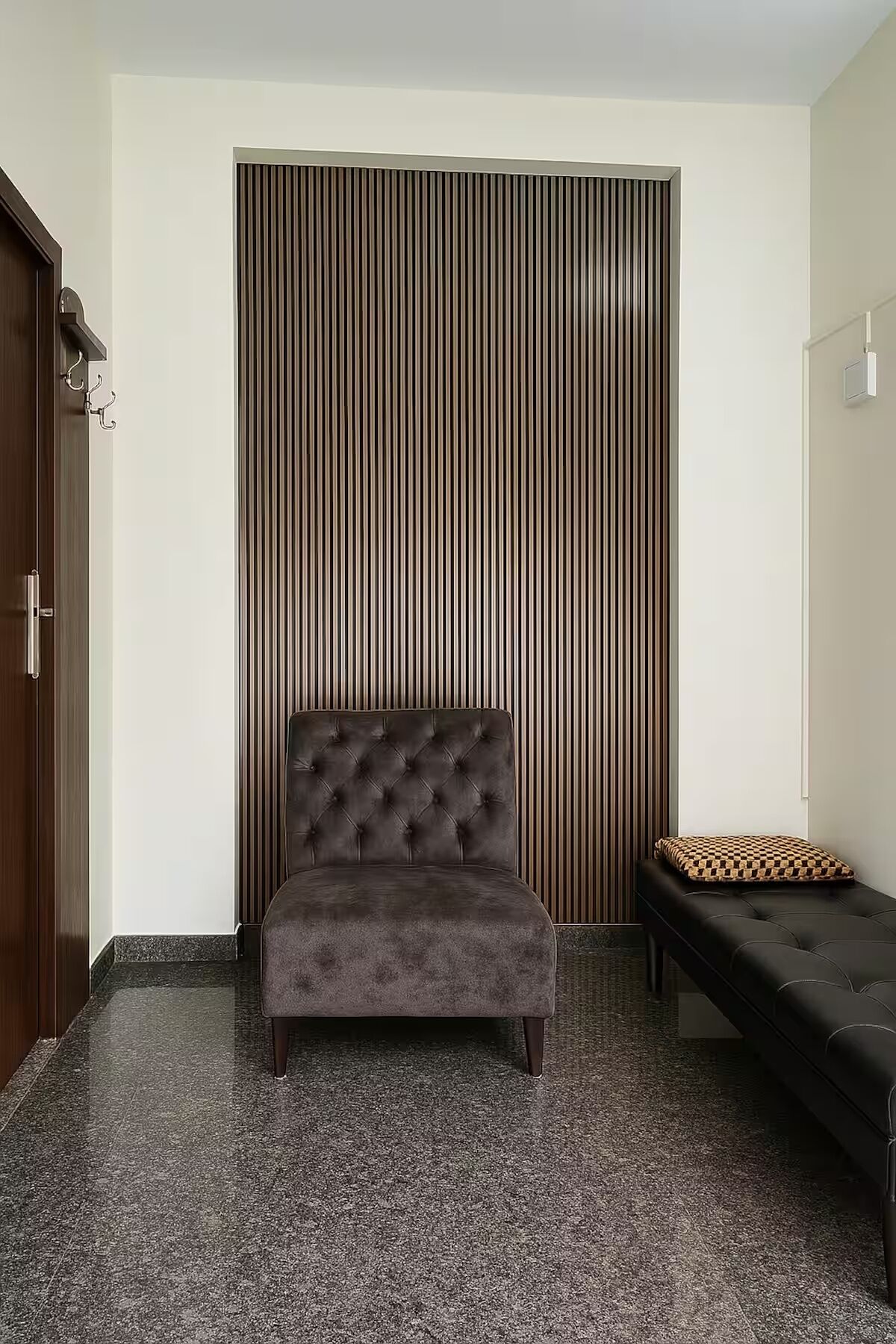 A room with a tufted sofa, a bench with a patterned cushion, and a vertical striped wall.