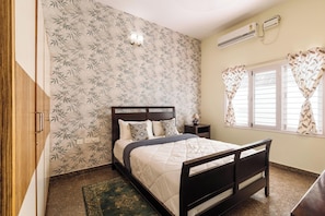 A bedroom with a bed, a nightstand, a wall-mounted air conditioner, and a window with curtains.