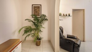 Eine Ecke eines Raumes mit einer Holzbank, einer Topfpflanze, einem gerahmten Kunstwerk an der Wand und einem Ledersofa im angrenzenden Raum.