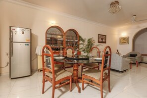 A dining area with a round table, wooden chairs, a refrigerator, and a glass cabinet with shelves.