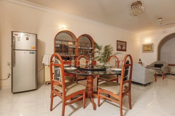 A dining area with a round table, wooden chairs, a refrigerator, and a glass cabinet with shelves.