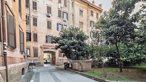 A multi-story building with a central courtyard, featuring a paved walkway and a small bridge. - Barbra Suite Testaccio (Roma)