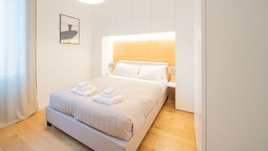 A neatly made bed with white linens and a quilted duvet, a bedside table with a lamp, and a framed picture on the wall. - Barbra Suite Testaccio (Roma)