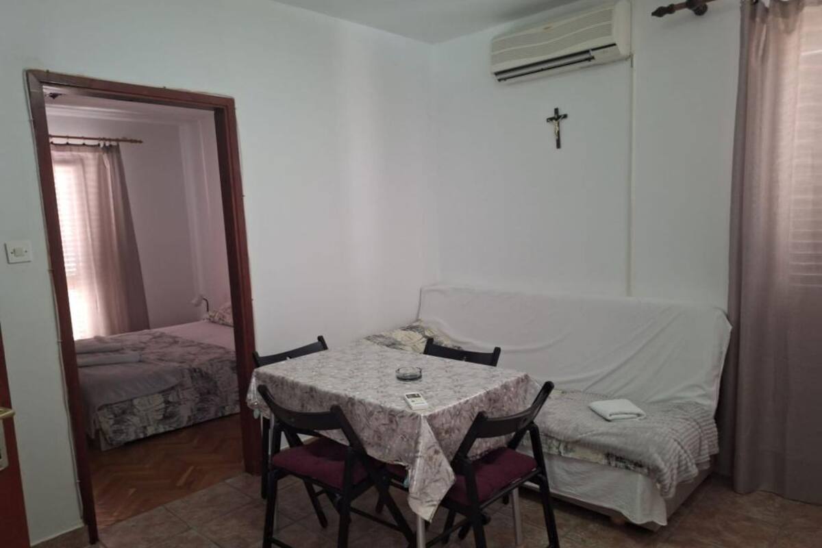 A small, single-room apartment with a dining table and chairs, a sofa, a bed, and a cross on the wall.