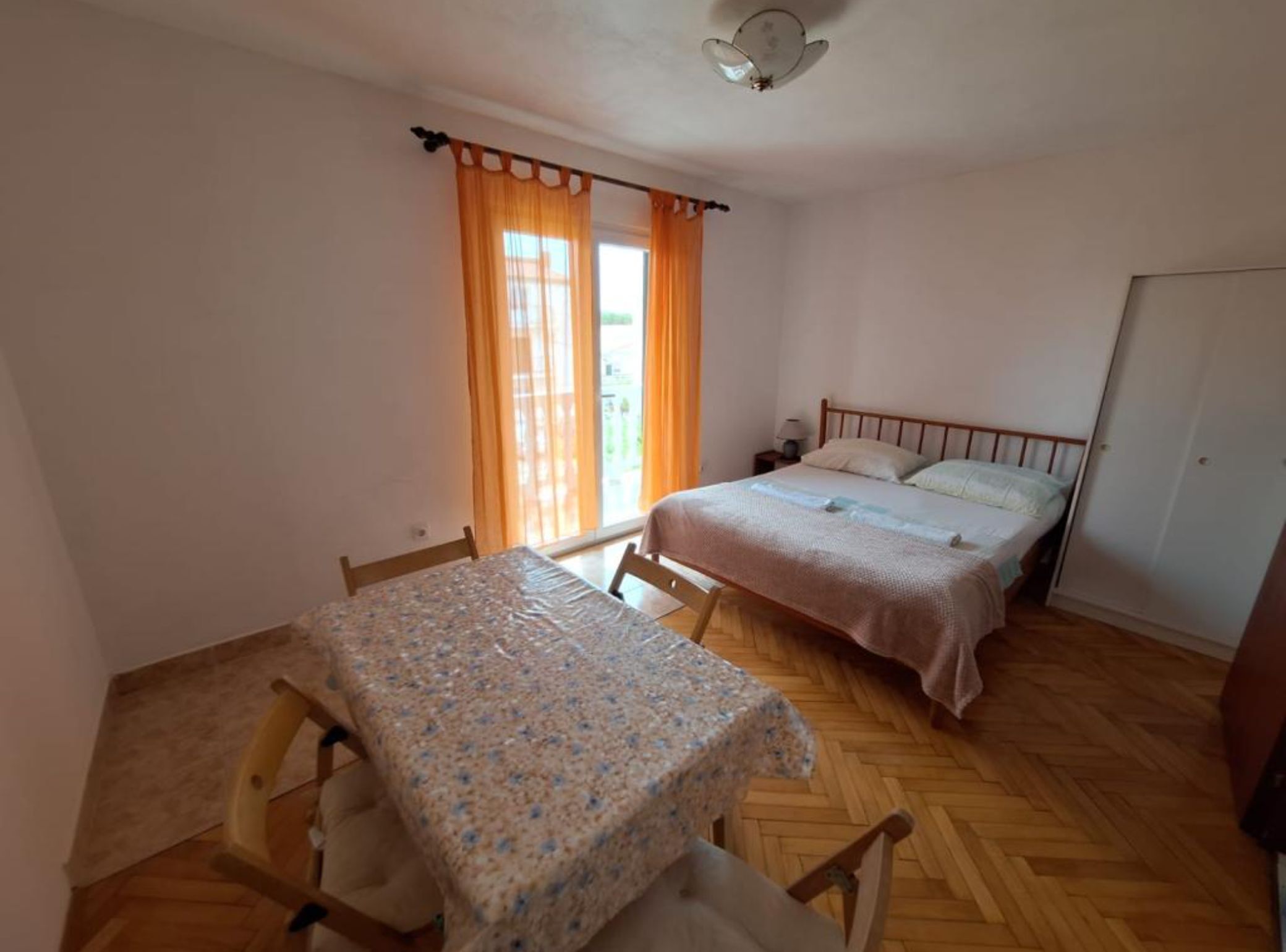 Ein Schlafzimmer mit Holzboden, einem Bett mit weißer Bettdecke, einem Nachttisch und einem Fenster mit Vorhängen.