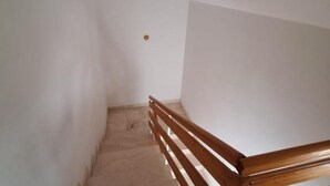 Una escalera con barandillas de madera, paredes blancas y un respiradero en el techo.
