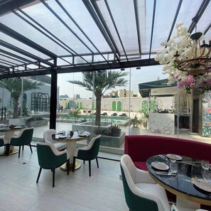 Un restaurante con techo de vidrio, mesas al aire libre y vistas a una piscina y edificios.