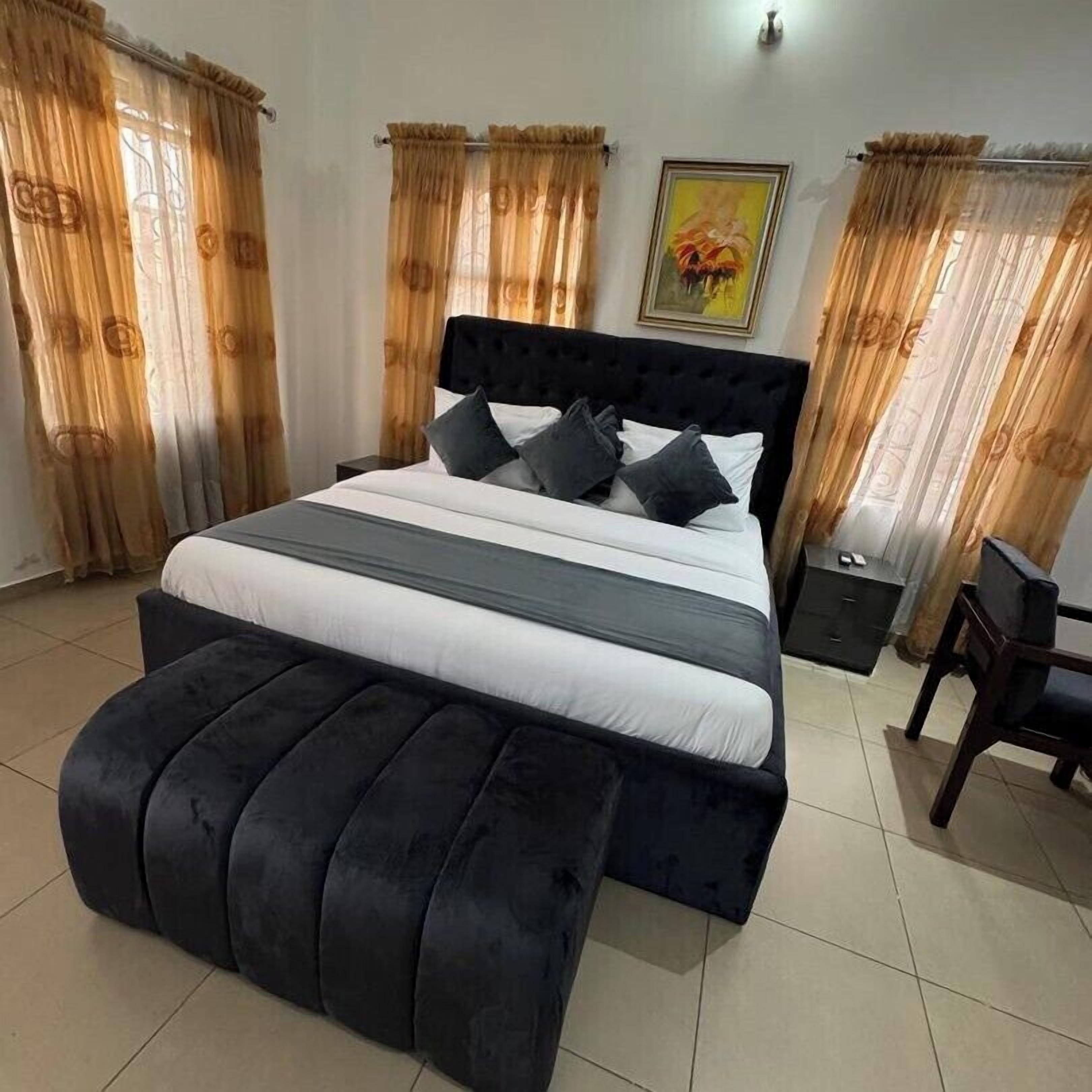 A bedroom with a large bed, a black upholstered bench, and curtains.