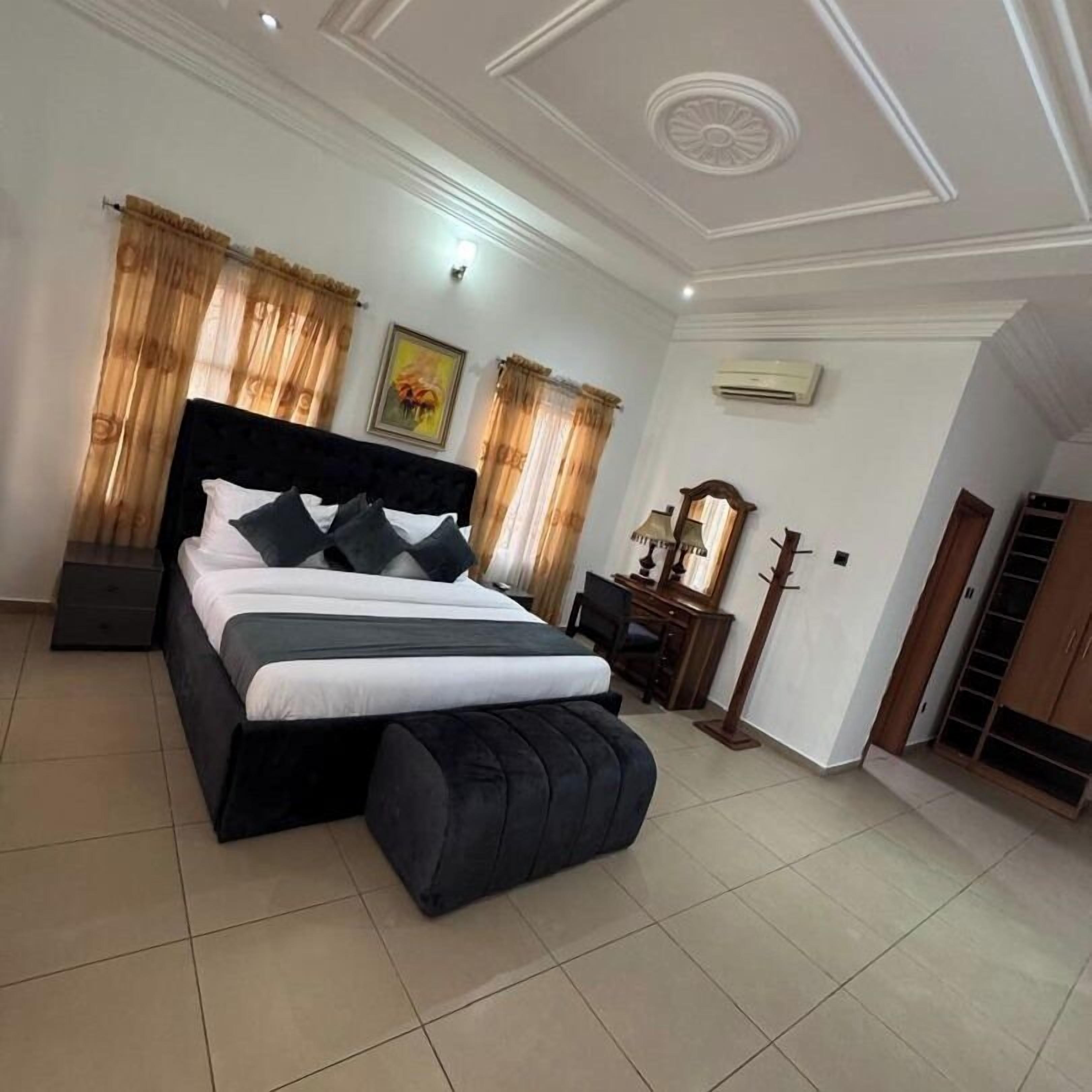 A bedroom with a large bed, a desk, a chair, a wardrobe, and an air conditioning unit.