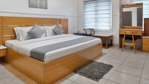 A modern bedroom with a wooden bed, bedside tables, a desk, and a chair. - The Breeze Apartment (Lagos)