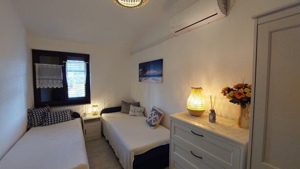A bedroom with two single beds, a nightstand with a lamp, a dresser, a window with lace curtains, and a painting on the wall. - Villa Hidden Gem (Bribir)
