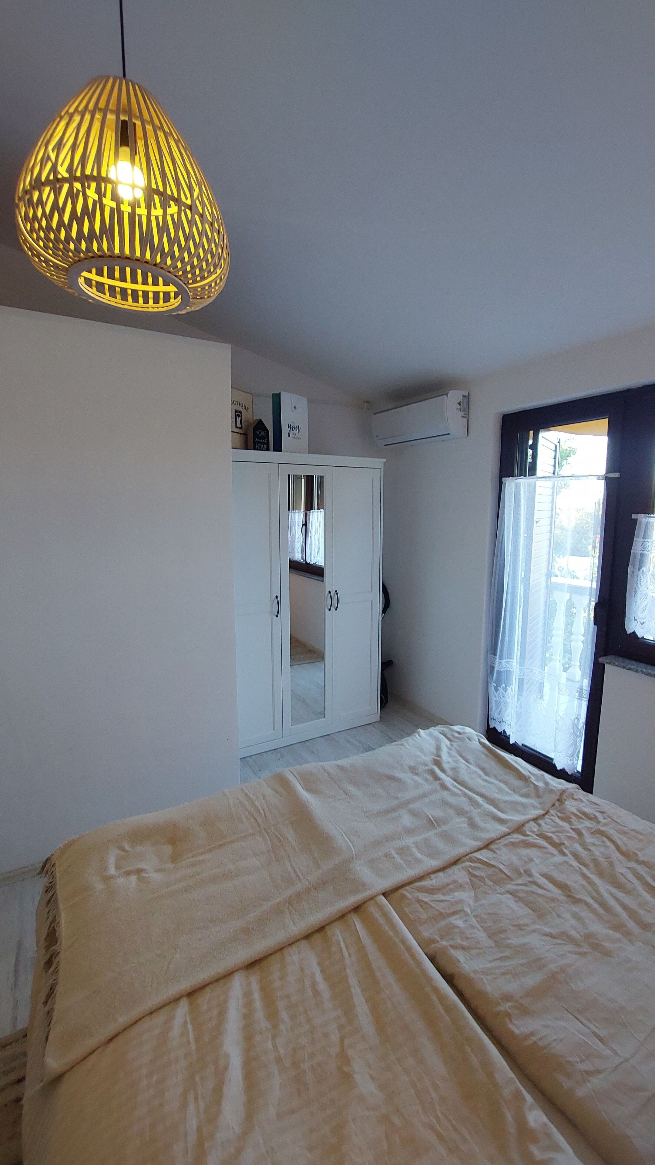 A bedroom with a bed, a hanging light fixture, a wardrobe, and a window with curtains.