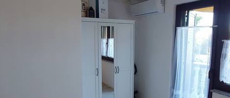 A bedroom with a bed, a hanging light fixture, a wardrobe, and a window with curtains.