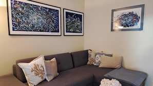 A modern living room with a grey sectional sofa, two abstract paintings, a glass coffee table with magazines, and a vase of flowers. - Villa Hidden Gem (Bribir)