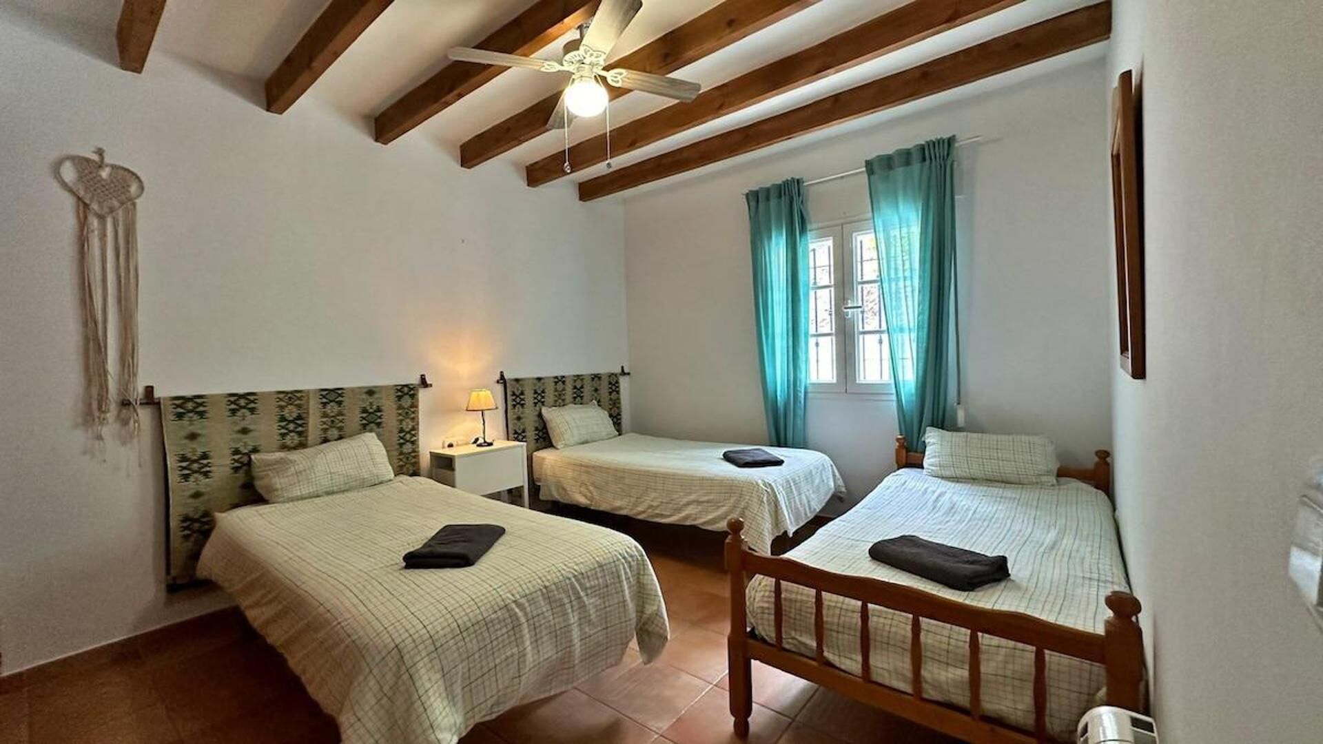 Una habitación con dos camas, ventilador de techo y ventana con cortinas.