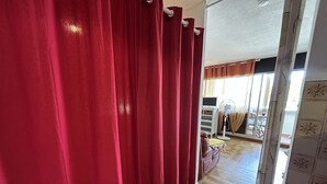 A room with red curtains, a fan, a bed, and a view of an outdoor balcony.