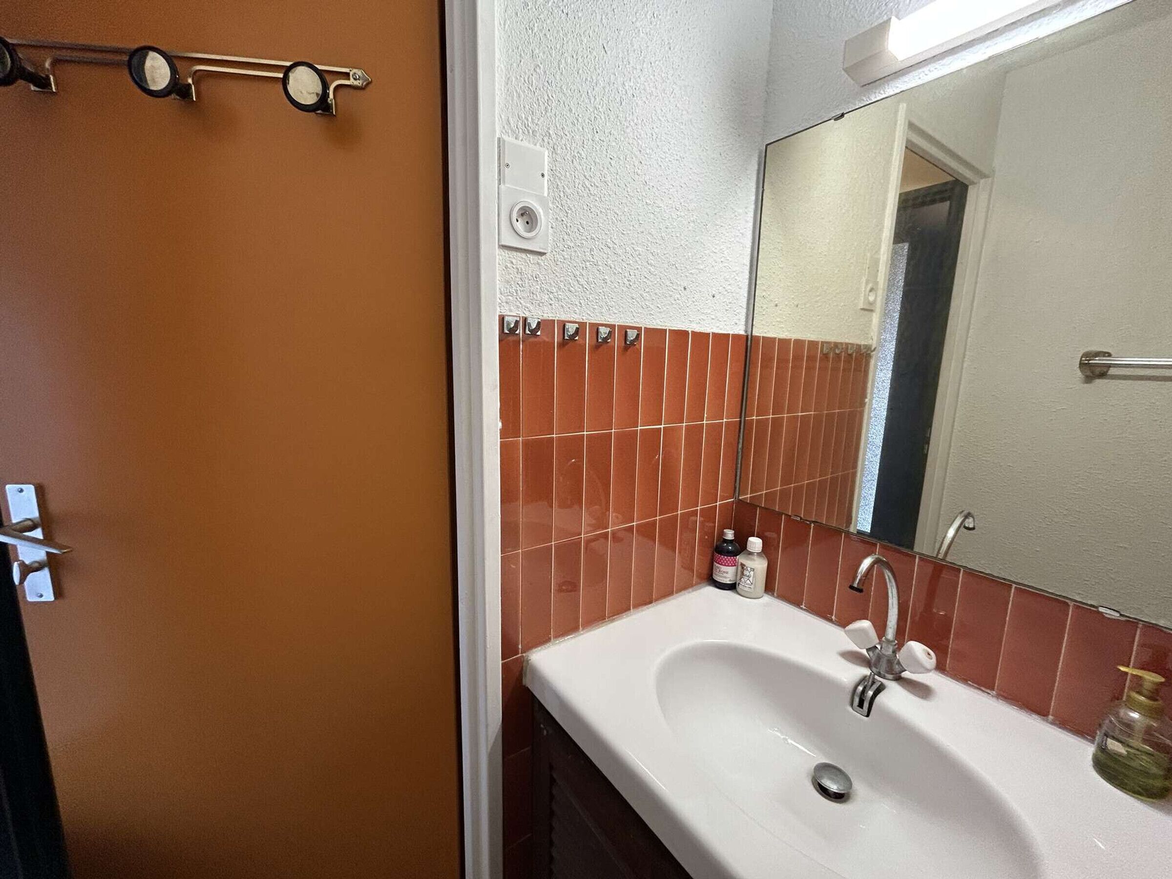 A bathroom with a white sink, red tiles, a mirror, and a towel rack.