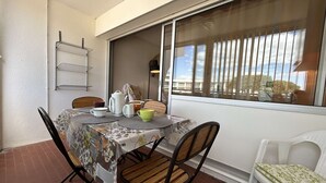A dining area with a table covered by a floral tablecloth, surrounded by chairs, and a window with blinds.