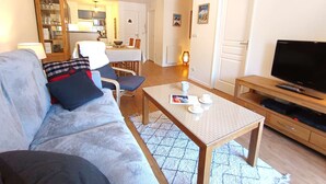 A living room with a sofa, a coffee table, a TV, and a dining area in the background.