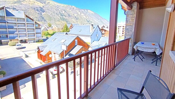 A balcony with a view of a mountain, a table with chairs, and a building with multiple windows.