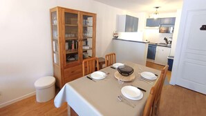 A dining area with a table set for four, a wooden cabinet with glass doors, and a kitchenette in the background.