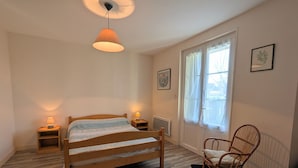 A bedroom with a wooden bed, two bedside tables with lamps, a chair, a window with curtains, and a radiator. - Cottage by the Creuse River with Private Garden (Ceaulmont)