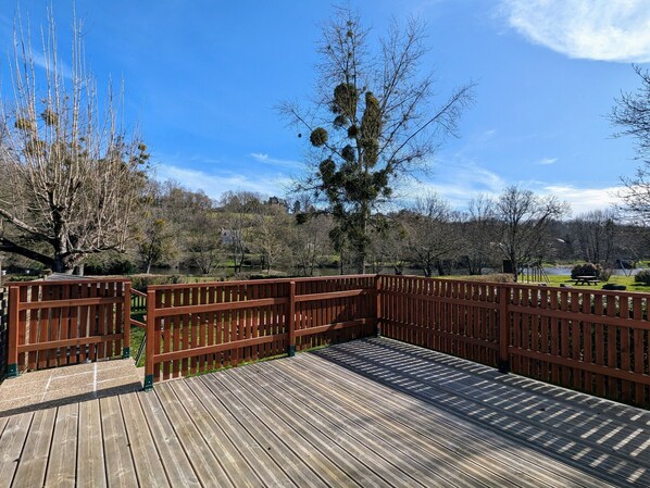A wooden deck with a railing, overlooking a lake and trees.