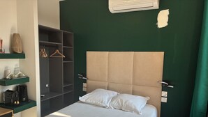 A neatly made bed with white linens and two pillows, a bedside table with a coffee maker, a hanging robe, and a wardrobe with shelves. - hôtel du Pharo (Marseille)