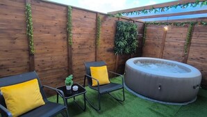 A wooden deck with a hot tub, two chairs with yellow cushions, and a small table with a potted plant. - The Infinite (Ribeira Grande)