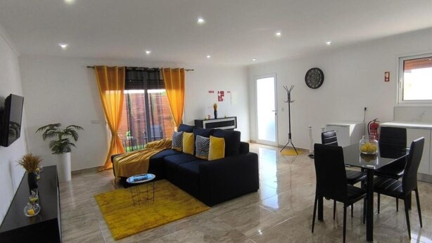 A modern living room with a sofa, coffee table, and dining area with chairs. - The Infinite (Ribeira Grande)