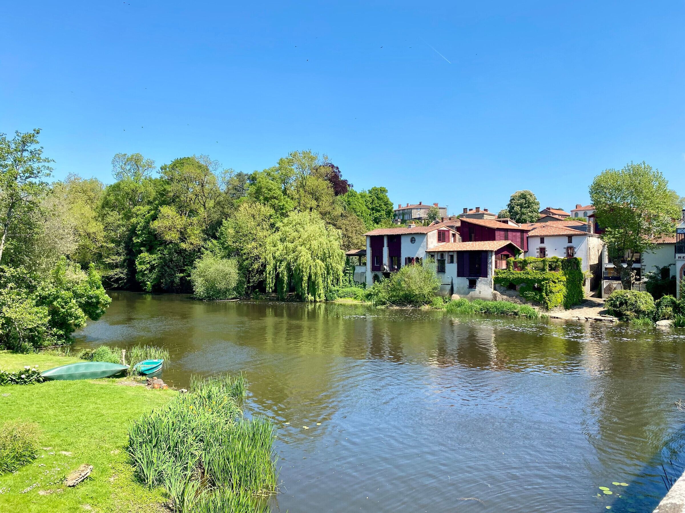 A riverside view with traditional buildings, a boat, and lush greenery.