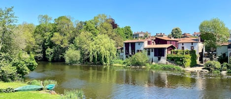A riverside view with traditional buildings, a boat, and lush greenery.