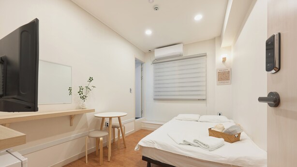 A hotel room with a bed, a desk with a chair, a small table, and a TV. - Dawoo House2 (Seoul)