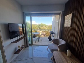 A modern living room with a flat-screen TV, a sofa, a wooden coffee table, and a balcony with a table and chairs.