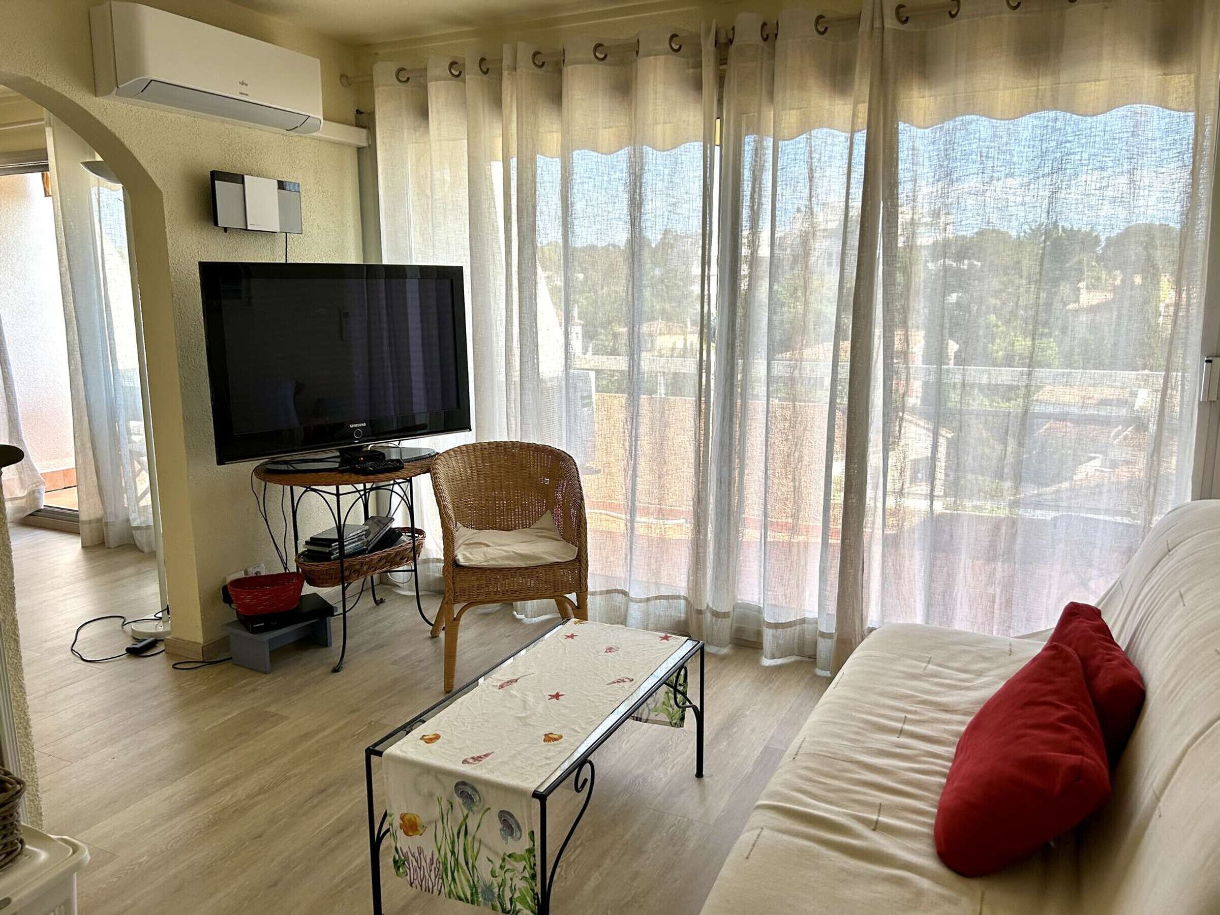 A living room with a TV, wicker chair, sofa, and a table with a floral tablecloth.