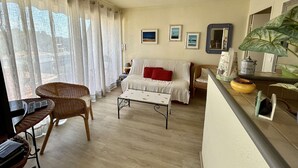 A living room with a sofa, a coffee table, a wicker chair, and a balcony with a plant. - Bright 2-room apartment, air-conditioned, near the sea in Saint-Raphaël (Saint-Raphaël)