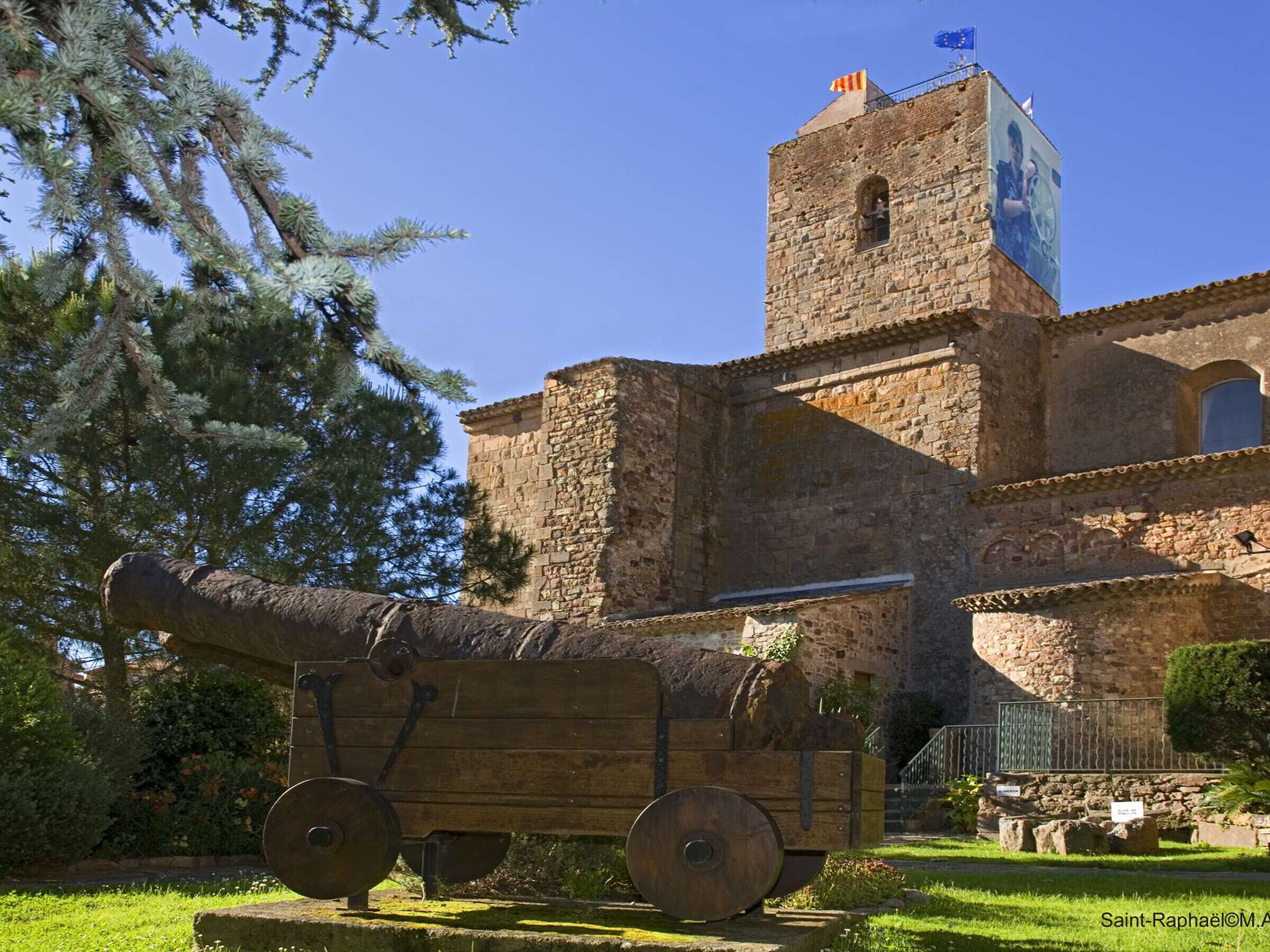 A historic stone building with a tower and a wooden cannon on display.