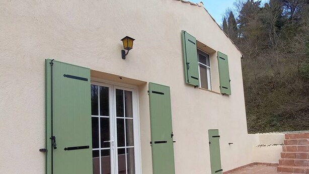 A building with a white exterior, green shutters, and a tiled patio area. - Provençal villa with garden and parking for 4 near Riez center (Riez)