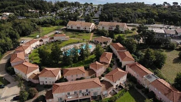Luftaufnahme eines Küstenresorts mit Villen mit Terrakotta-Dächern, einem zentral gelegenen Schwimmbad und dem Meer im Hintergrund.