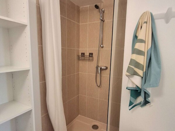 A shower area with a glass door, a towel rack with a towel, and white shelving units.